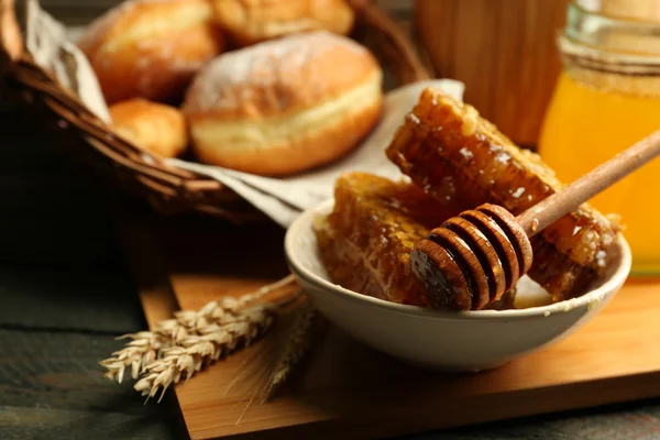 Honingraten op plaat, warme broodjes in mand op houten achtergrond — Stockfoto