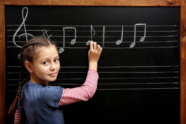 Menina escrevendo no quadro negro com notas musicais — Fotografia de Stock