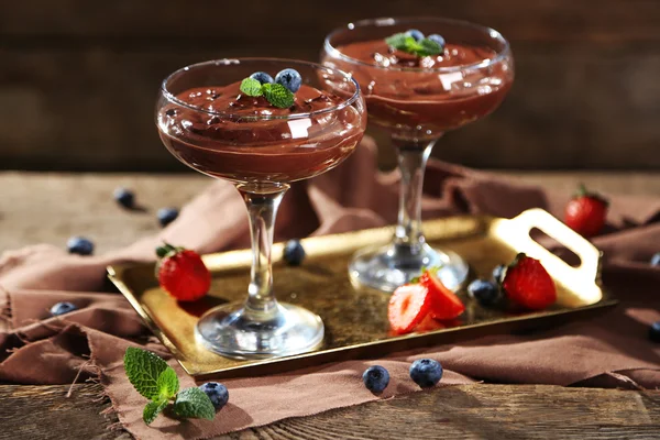 Schokoladendessert in Gläsern und frischen Beeren auf farbigem Holzhintergrund — Stockfoto