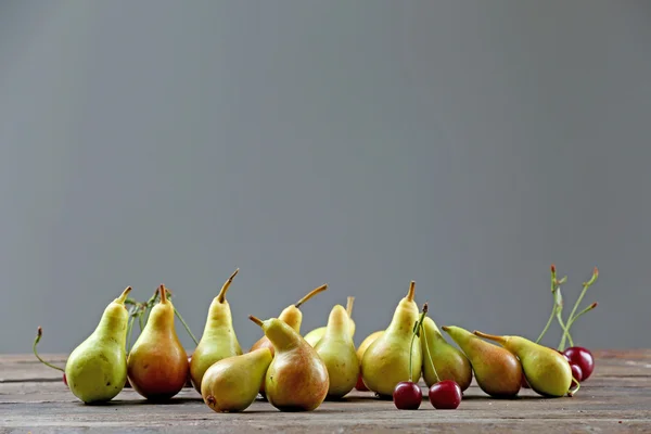 Reife Birnen und Kirschen auf grauem Hintergrund — Stockfoto