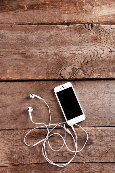 Celular branco com fones de ouvido em fundo de madeira — Fotografia de Stock