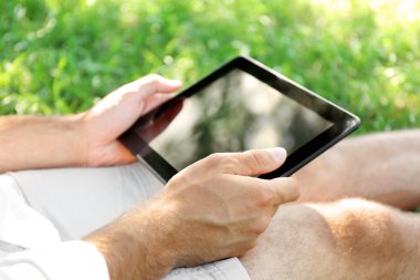 Adam yeşil çimenlerin üzerinde oturan tablet ile 