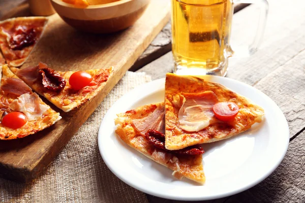Sliced pizza served with beer on wooden table — Stock Photo, Image