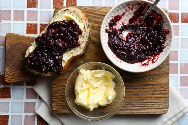 Tasty jam on the plate, butter in a bowl, bread on wooden tablet and a napkin on mosaic background — Stock Photo, Image