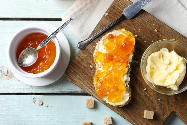 Marmellata saporita nel barattolo e nelle ciotole, burro, pane fresco e cracker su fondo di legno blu — Foto Stock