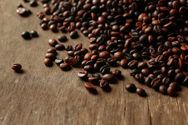 Grãos de café aromáticos espalhados no fundo de madeira — Fotografia de Stock
