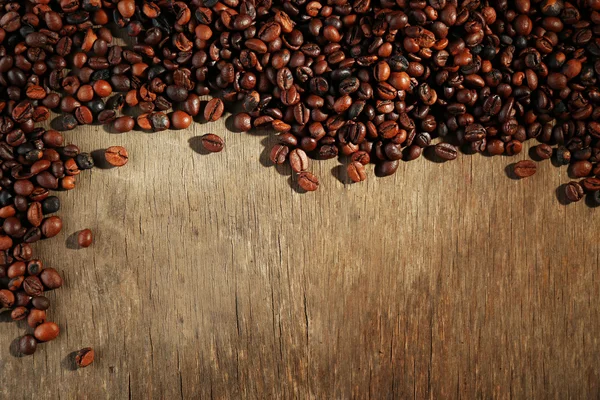 Aromatische Kaffeebohnen auf Holzgrund verstreut — Stockfoto