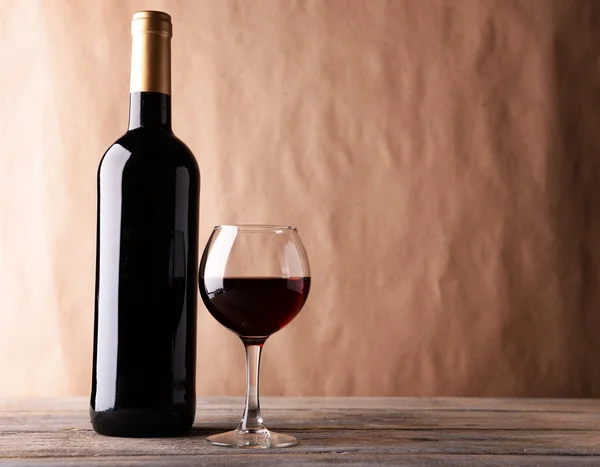 Una botella de vino tinto y una copa sobre una mesa de madera — Foto de Stock