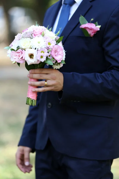 Venku drží svatební kytici ženich — Stock fotografie