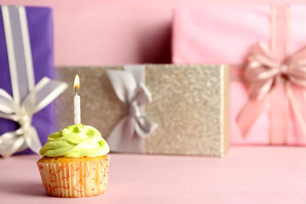 Sabroso cupcake con vela sobre mesa rosa sobre coloridas cajas de regalo fondo — Foto de Stock