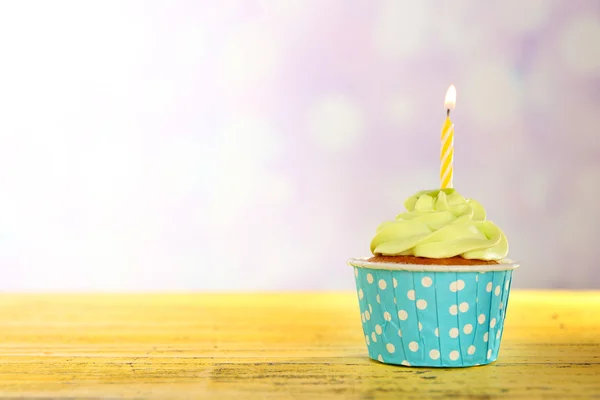 Sabroso cupcake con vela sobre mesa de madera amarilla sobre fondo desenfocado —  Fotos de Stock