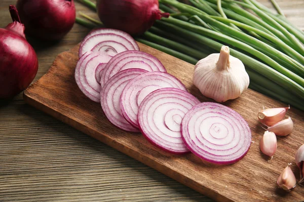 Červená cibule kruhy, zelené cibule s česnekem na palubě dřevěné pozadí — Stock fotografie