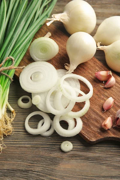 Onions circles, fresh green onion with garlic on board against wooden background — Stock Photo, Image