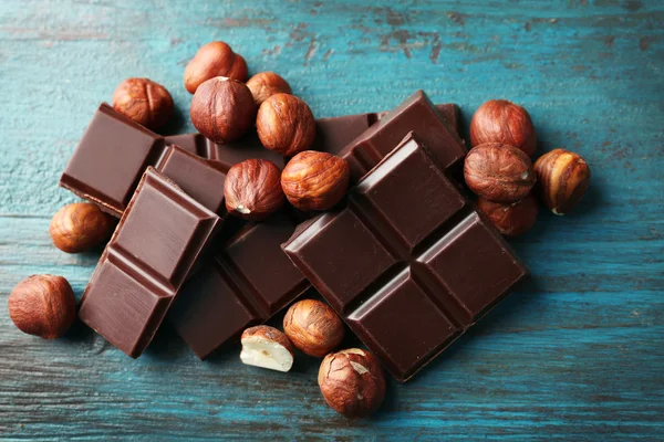 Piezas de chocolate negro con nueces sobre fondo de madera de color —  Fotos de Stock