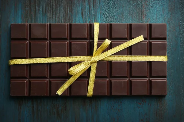 Barra di cioccolato fondente con fiocco colorato su sfondo di legno colore — Foto Stock