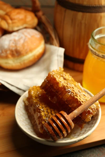 Waben auf Teller, heiße Brötchen im Korb auf Holzgrund — Stockfoto