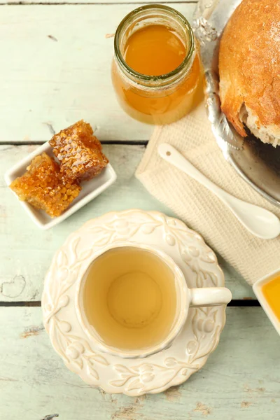 Wabe, Schüssel mit Honig, Tasse mit Kräutertee auf farbigem Holzhintergrund — Stockfoto