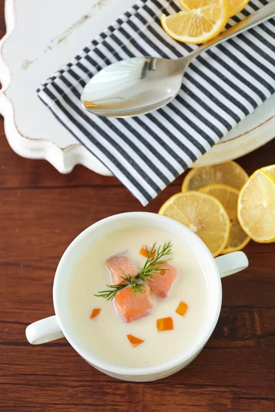 Délicieuse soupe à la crème de saumon dans un bol blanc au citron et serviette en coton rayé sur une table en bois, fermer — Photo