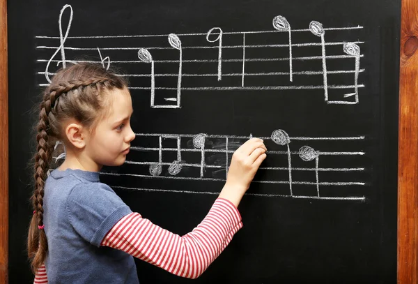 Chica escribiendo en pizarra notas musicales — Foto de Stock