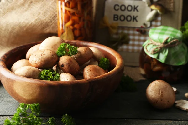 Mushrooms in wooden bowl and marinated mushrooms in jar on wooden surface — Stock Photo, Image