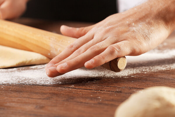 Hands rolling dough basis for pizza