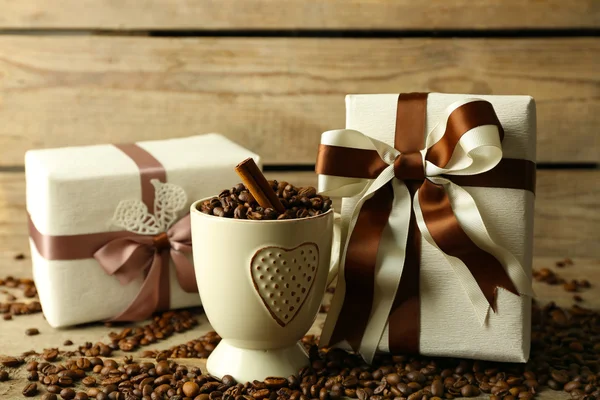 Beautiful gift with bow and coffee grains in mug, on wooden background — Stock Photo, Image