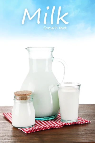 Кувшин, банка и стакан молока на светло-голубом фоне — стоковое фото