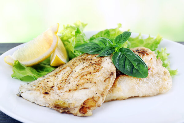 Dish of fish fillet with greens and lemon on bright background