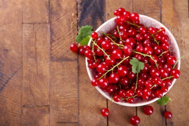 Ahşap masa üzerinde kase taze kırmızı kuş üzümü yakın çekim