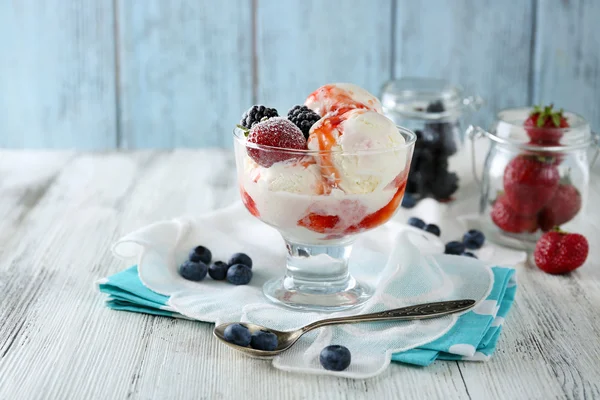 Вкусное мороженое со свежими замороженными ягодами и соусом, на фоне цвета дерева — стоковое фото