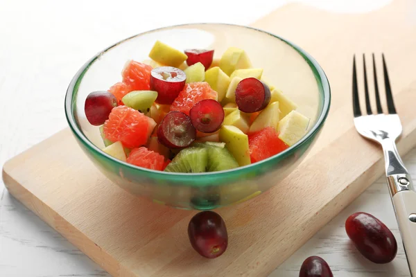 Insalata di frutta in ciotola di vetro, su fondo di legno chiaro — Foto Stock