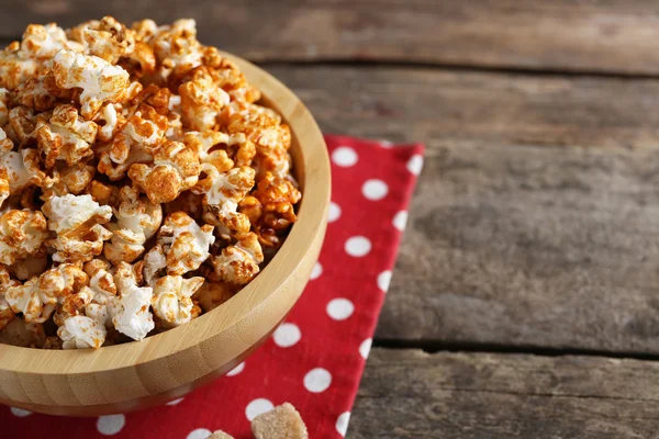 Zoete karamel popcorn in een kom op rode katoen servet tegen houten achtergrond — Stockfoto