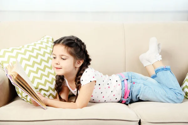 Menina deitada no sofá com livro — Fotografia de Stock