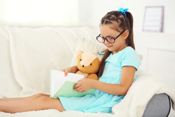 Bambina seduta sul divano con libro — Foto Stock