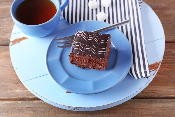 Sweet chocolate cake on blue plate with cup of tea on wooden table — Stock Photo, Image