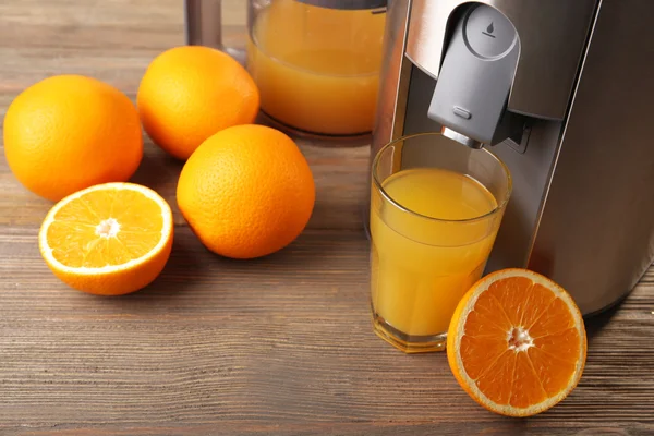 Stainless juice extractor with glass of orange juice on wooden background, close up — Stock Photo, Image