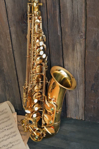 Beautiful golden saxophone with musical notes on wooden background, close up — Stock Photo, Image