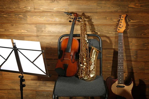 Musical instruments on a chair and note holder against wooden background — Stock Photo, Image