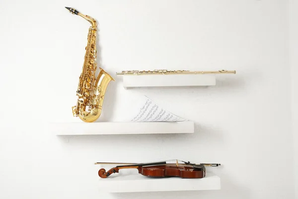 Violín, flauta y saxofón sobre estantes decorados sobre fondo blanco de pared — Foto de Stock