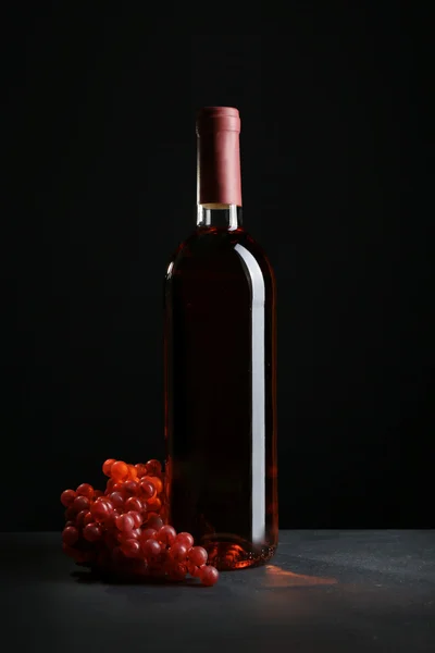 Butelkę wina i czerwone winogrona, na tle szaro czarny — Zdjęcie stockowe