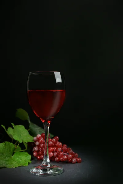 Un verre de vin et de raisins rouges, sur fond gris-noir — Photo