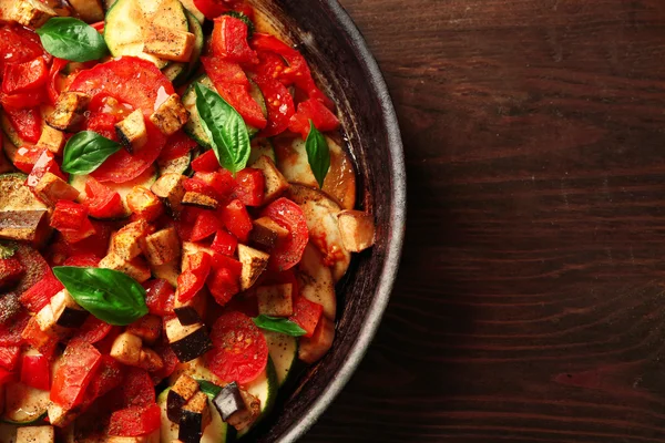 Tasty vegetarian ratatouille made of eggplants, squash, tomatoes and onions in black cast iron pan, on wooden table background — Stock Photo, Image