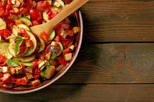 Вкусный вегетарианский рататуй из баклажанов, сквоша, помидоров и лука в черной чугунной сковороде, на деревянном фоне стола — стоковое фото