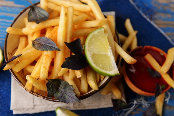 Frans gebakken aardappelen in kom met basilicum en saus op oude houten achtergrond — Stockfoto