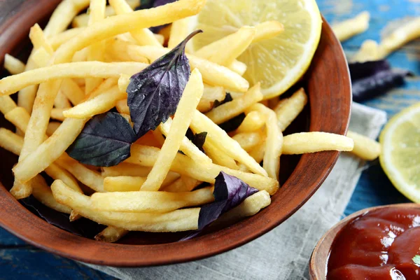 French fried potatoes in bowl with basil and sauce on old wooden background — Stock Photo, Image