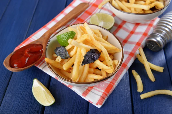 French fried potatoes in bowl with basil and sauce on old wooden background — Stock Photo, Image