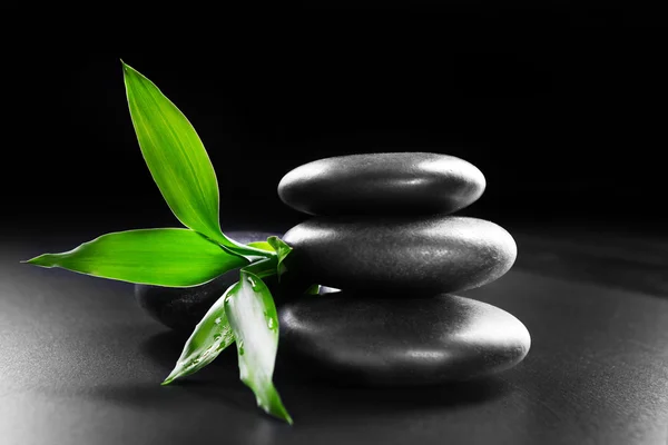 Pile of pebbles with bamboo leaf on black background — Stock Photo, Image