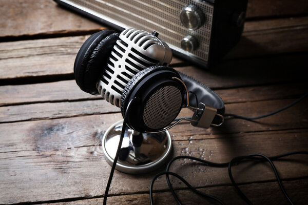 Microphone with headphones and radio on wooden background