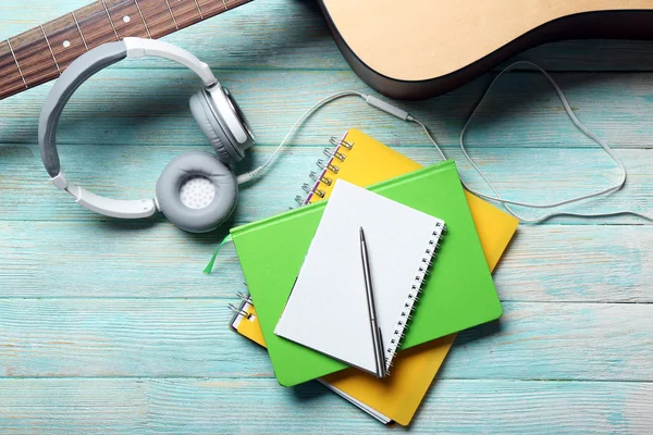 Hoofdtelefoon met gitaar en notebook op blauwe houten achtergrond — Stockfoto