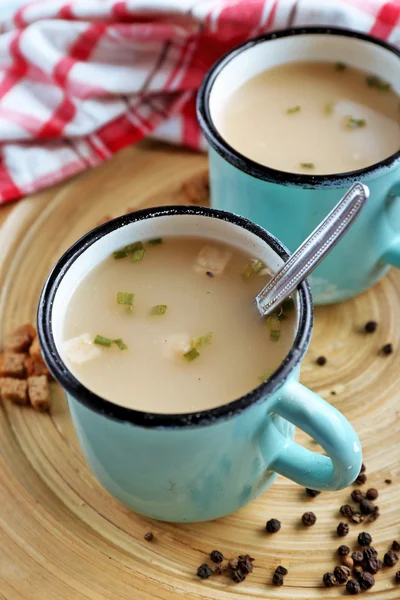 Mugs of soup on wooden mat closeup — Stock Photo, Image